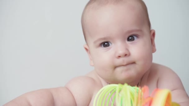 Infância, infância, paternidade, desenvolvimento, medicina e conceito de saúde - visão frontal close-up nu gordinha recém-nascido criança alegre vigília em terno rosa sorrindo com brinquedo multicolorido deitado na barriga — Vídeo de Stock