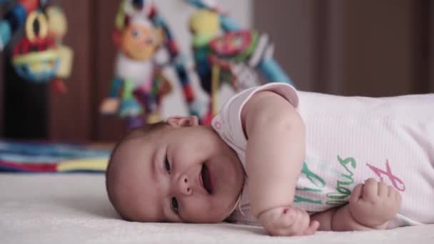 Kojenectví, dětství, rodičovství, vývoj, medicína a zdraví koncept - boční pohled close-up tvář baculaté novorozeně dítě radostné probuzení v růžové kombinéze s úsměvem a dělat grimasy ležící na břiše — Stock video