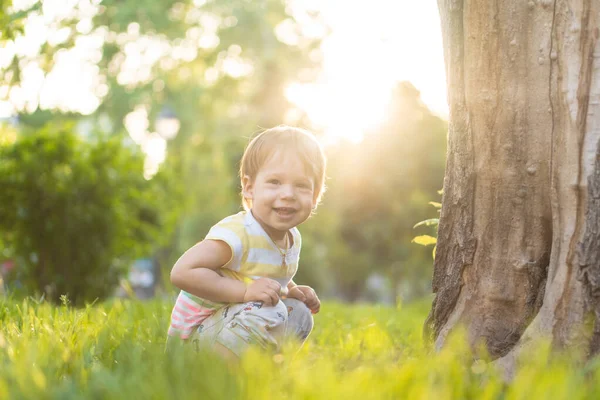 Παιδική ηλικία, τη φύση, το καλοκαίρι, πάρκα και σε εξωτερικούς χώρους έννοια - πορτρέτο του χαριτωμένο ξανθά μαλλιά μικρό αγόρι σε ριγέ πολύχρωμο T-shirt με serous, λυπηρό βλέμμα στο παρασκήνιο του ηλιοβασιλέματος στο πάρκο. Αντιγραφή χώρου. — Φωτογραφία Αρχείου