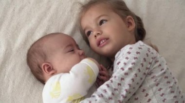 Çocukluk, çocukluk, aile, uyku, dinlenme konsepti - iki mutlu çocuğa yakın çekim, yeni doğan bebek ve 3-4 yaşındaki kız bej ve beyaz yatakta uzanıyorlar. Kız kardeşler evdeki kanepede oynuyorlar..