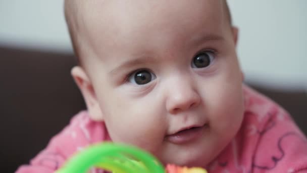 Infância, infância, paternidade, desenvolvimento, medicina e conceito de saúde - visão frontal close-up rosto gordinho recém-nascido bebê alegre vigília em terno rosa sorrindo com brinquedo multicolorido deitado na barriga — Vídeo de Stock