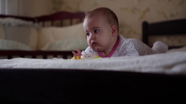 Kojenectví, dětství, rodičovství, vývoj, medicína a zdraví koncept - pohled zepředu close-up tvář baculaté novorozeně dítě radostné bdění v růžové kombinéze úsměv s pestrobarevnou hračkou ležící na břiše — Stock video