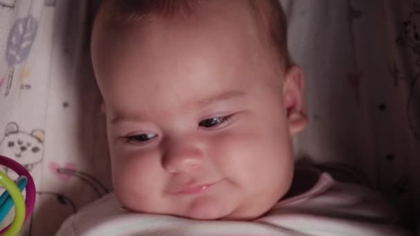 Sugari, copilărie, concept de emoție - închiderea feței zâmbitoare drăguțe a nou-născutului dolofan cu ochi căprui, treaz, fără dinți, de 7 luni, uitându-se la aparatul de fotografiat culcat în costum de corp alb cu dinți mari în cărucior — Videoclip de stoc