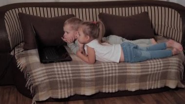 Aile, oyun, karantina, çocukluk kavramları iki mutlu çocuk karantina sırasında evdeki kahverengi kanepede dizüstü bilgisayar izleyip çizgi film izliyor. Çocuklar erkek kardeşler, kız kardeşler birlikte eğlenin.