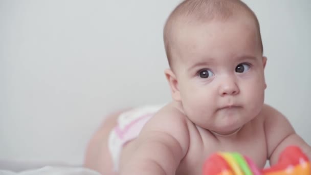 Infância, infância, paternidade, desenvolvimento, medicina e conceito de saúde - visão frontal close-up nu gordinha recém-nascido criança alegre vigília em terno rosa sorrindo com brinquedo multicolorido deitado na barriga — Vídeo de Stock