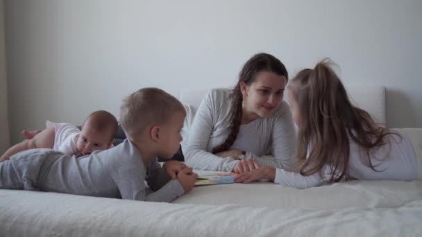 Niñez, maternidad, concepto de hermanos - Despreocupada joven mamá leer libro colas de hadas para los niños pequeños, hijo recién nacido divertirse jugar en la cama, feliz alegre familia risa cosquillas, beso, abrazos mintiendo relajarse — Vídeos de Stock