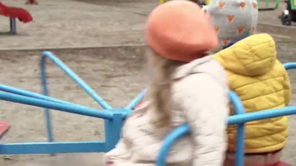 Dzieciństwo, rodzina, macierzyństwo, koncepcja zimowa - Dwa przedszkola nieletni chłopiec i dziewczynka 2-4 lat brat i siostra bawią się na placu zabaw w jesiennym parku. małe dzieci na karuzeli siedzi w pobliżu — Wideo stockowe