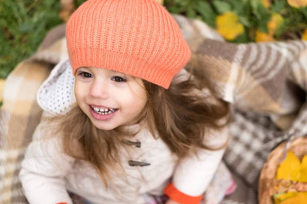 Παιδική ηλικία, οικογένεια, νήπιο, μητρότητα, φθινοπωρινή έννοια - top view Μικρό χαμογελαστό χαρούμενο χαριτωμένο προνήπιο μικρό ξανθό κορίτσι σε πορτοκαλί μπερέ κάθεται σε καρό με κίτρινα πεσμένα φύλλα σε κρύο καιρό στο πάρκο — Φωτογραφία Αρχείου