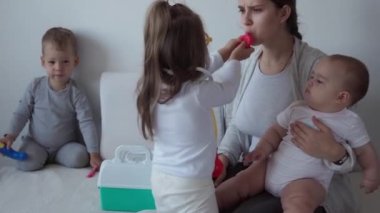 Tıp, aile, oyun konseptleri, konsantre oyun oynayan çocuklar tıbbi gözlük takıyor. Doktor gibi davran, hemşire ol, dinle gülümse anne yeni doğmuş bebek kız kardeşin derin nefes al, yatağa otur.