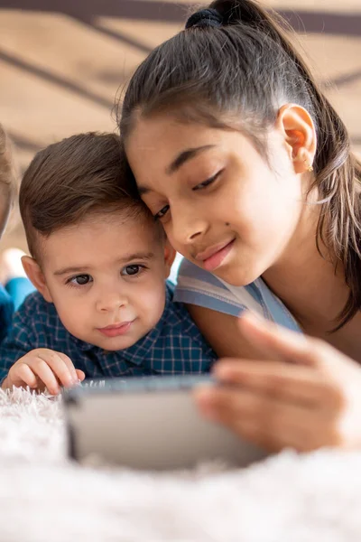 Φιλία, την παιδική ηλικία, την τεχνολογία έννοιες - 2 μικρά παιδιά μωρό διαφορετικών εθνικοτήτων περσική και σλαβική εμφάνιση παρακολουθήσουν κινούμενα σχέδια στο smartphone στο κρεβάτι. παιδιά προσχολικής ομιλίας από το βίντεο συνέδριο — Φωτογραφία Αρχείου