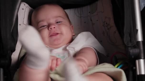 Niemowlę, dzieciństwo, koncepcja emocji - zbliżenie uśmiechniętej twarzy brązowookiego pulchnego noworodka budzącego się bezzębnego dziecka w wieku 7 miesięcy patrzącego na kamerę leżącą w białym body z kolorowymi paskami w wózku — Wideo stockowe