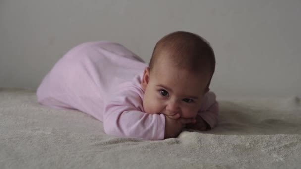 Bebek, çocukluk konsepti, gülümseyen mutlu tombul, kahverengi gözlü, yeni doğmuş çocuğun tombul yüzünün yakın çekimi. Dişsiz 7 ay bebek buruşuklukları, gözlerini kapatır yumuşak yatağa uzanır pembe kemiren parmaklar yatakta — Stok video