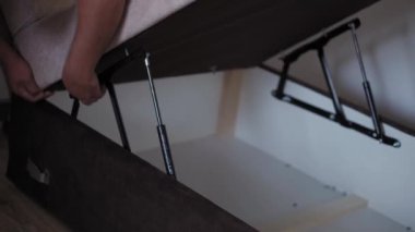 Yenileme, inşaat konsepti. Yakın plan, el kamerası çekimleri. Mobilyaları büken matkapla erkek eli. Adamın biri evdeki yatak odasında kanepe topluyor..