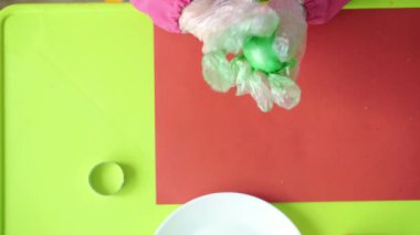 Paskalya, Hamursuz Bayramı, çocukluk, yaratıcılık, oyun konsepti - Sloven beyaz önlüklü üç yaşındaki tatlı sarışın kızın yakın çekimi plastik eldivenle Paskalya yumurtalarını boyuyor.