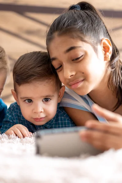 Φιλία, την παιδική ηλικία, την τεχνολογία έννοιες - 2 μικρά παιδιά μωρό διαφορετικών εθνικοτήτων περσική και σλαβική εμφάνιση παρακολουθήσουν κινούμενα σχέδια στο smartphone στο κρεβάτι. παιδιά προσχολικής ομιλίας από το βίντεο συνέδριο — Φωτογραφία Αρχείου