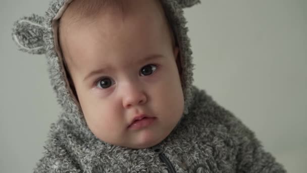 Uczucia, emocje, dzieciństwo, koncepcje macierzyństwa - słodkie, zdenerwowane dziecko w wieku 8 miesięcy patrz przed kamerę. zbliżenie mało smutne płacz dziecko czuje ból ząbkowanie w ciepłym szarym swetrze z kapturem wewnątrz — Wideo stockowe