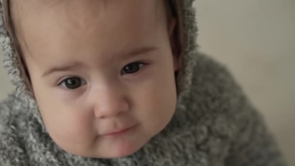 Feelings, emotions, childhood, motherhood concepts - Beautiful funny smiling kid baby aged 8 months look at camera. Awake minor happy anxious infant child in warm gray sweater with hood sit on bed — Stock Video