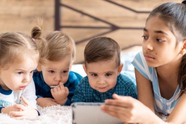 Arkadaşlık, çocukluk, teknoloji kavramları. Farklı milletlerden 4 çocuk. Farsça ve Slav görünümlü bebekler. Çocuklar anaokulunda video konferansına göre konuşuyor