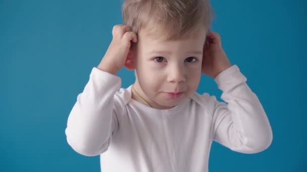 Відеозйомка, щастя, концепції дитинства - щаслива, усміхнена, радісна дитина дошкільного немовляти Тоддлер здивувала блондинку, яка позує на камеру на синьому фоні. Сексуальні емоції маленької радості дитини — стокове відео
