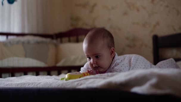 Infanzia, infanzia, genitorialità, sviluppo, medicina e concetto di salute - vista frontale primo piano viso paffuto neonato gioiosa veglia in body rosa sorridente con giocattolo multicolore sdraiato sulla pancia — Video Stock