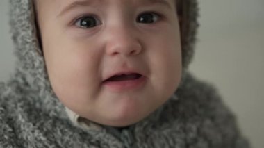 Duygular, duygular, çocukluk, annelik kavramları - 8 aylık sevimli üzgün bebek kameraya bak. Kapüşonlu sıcak gri süveterin içinde diş çıkartan küçük, üzgün bir çocuk gibi ağla.