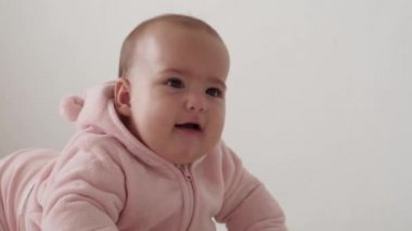 Bebek, çocukluk konsepti, gülümseyen mutlu tombul, kahverengi gözlü, yeni doğmuş çocuğun tombul yüzünün yakın çekimi. Dişsiz 7 aylık bebek buruşuklukları, gözlerini kapatır yumuşak yatağa uzanmış pembe taklalar içinde karın üstü yatar..