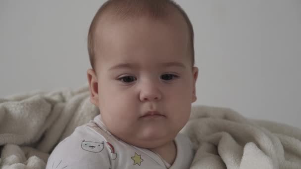 아기, 유아 개념 - 행복 한 갈색 눈을 가진 행복 한 아기가 깨어 있는 모습을 가까이서 미소짓는 것. 7 개월된 아기의 얼굴을 감싼 채 따뜻 한 담요에 싸인 부드러운 침대 위에 눈을 감고 있는 아기의 모습 — 비디오
