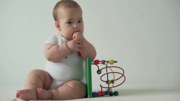 Bébé, concept d'enfance heureux drôle tout-petit enfant 8 mois bébé fille lécher jouer en bois Wired Bead Maze Abacus jeu sur fond blanc. chubby éveillé mineur assis rongeant jouet dans la salle de jeux à l'intérieur à la maison — Video