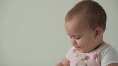 Bebek, çocukluk konsepti. Gülümseyen mutlu kahverengi gözlü, tombul çocuk uyandı. Neşesiz, dişsiz, 7 aylık bebek buruşuklukları, gözlerini kapatır evdeki beyaz arka planda yumuşak yatağa oturur.