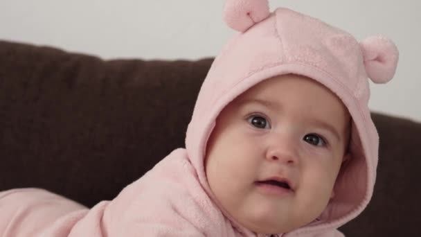 Infant, childhood concept - close-up of smiling happy plump funny portrait brown-eyed chubby face of newborn kid awake. toothless 7 month baby grimaces, closes eyes lie on soft bed in pink on tummy. — Stock Video