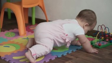 Bebek, çocukluk konsepti. Mutlu, komik, küçük bir çocuk. 8 aylık bebek kız, oturup tahta ve kablo boncuklu abaküs oyunu oynuyor. Tombul uyanık yeni doğmuş bebek oyun odasında, evde yerde sürünüyor.