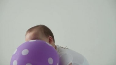 Bebek, çocukluk konsepti. Mutlu çocuk oyuncağı. 8 aylık bebek doğum günü partisinde mor balonla oynuyor. gülümseyen tombul aktif uyanıkken dizlerinin üzerinde sürünerek evde beyaz arka planda