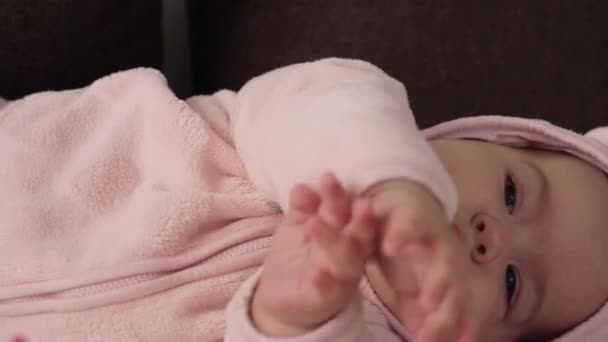 Младенческая, детская концепция - крупным планом улыбающегося веселого пухлого смешного пухленького лица новорожденного ребенка в сознании. беззубый 7 месяцев ребенок гримасы, закрывает глаза лежат на мягкой кровати в розовых грызут пальцы на кровати — стоковое видео