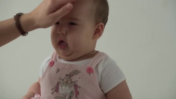 Criança, infância, higiene, maternidade, conceito de cuidado - close-up de sorrir rosto gordinho de olhos castanhos feliz de criança pequena acordada. mãe pentes engraçado criança filha com escova de cabelo no fundo branco em casa. — Vídeo de Stock