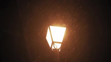 Hava tahmini, anormallik, acil durum, element, kış konsepti. Kar yağışının sabit olmayan el kamerasıyla çekilmesi. Gece parkındaki sokak lambalarının sarı ışığında düşen kar taneleri. Kiev 'deki ilk kar
