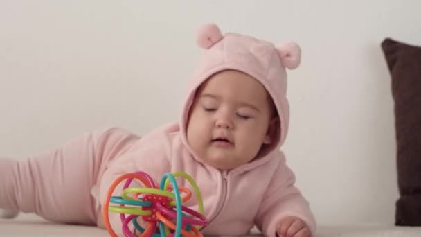 Niemowlę, koncepcja z dzieciństwa - zbliżenie uśmiechniętej szczęśliwej pulchnej, zabawnej brązowookiej, pulchnej twarzy noworodka obudzonego. bezzębny 7 miesięcy grymas dla dzieci, zamyka oczy leżą na miękkim łóżku w różowym z gryzakiem w domu — Wideo stockowe