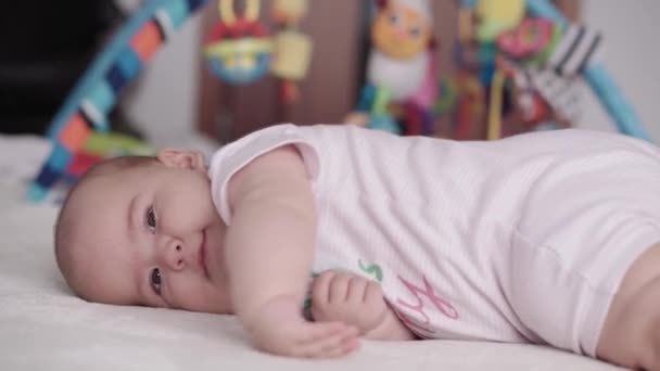 Kojenectví, dětství, rodičovství, vývoj, medicína a zdraví koncept - boční pohled close-up tvář baculaté novorozeně dítě radostné probuzení v růžové kombinéze s úsměvem a dělat grimasy ležící na břiše — Stock video