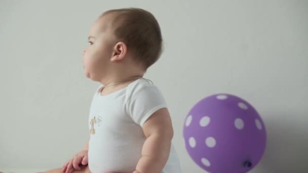 Bebé, concepto de la infancia - niño pequeño juguetón divertido feliz niño de 8 meses niña jugar con el globo púrpura en fiesta de cumpleaños. sonriente gordito activo despierto gatear en rodillas dentro en casa en blanco fondo — Vídeos de Stock