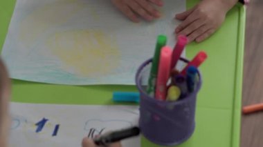 Sanat, eğitim, çocukluk, kavramlar- Küçük mutlu bir ilkokul anaokulu küçük küçük çocuk keçeli kalem ve kalemlerle çizim yapıyor kapalı bir masada oturuyor. gülümseyen çocuklar kapalı alanda resim yapar.