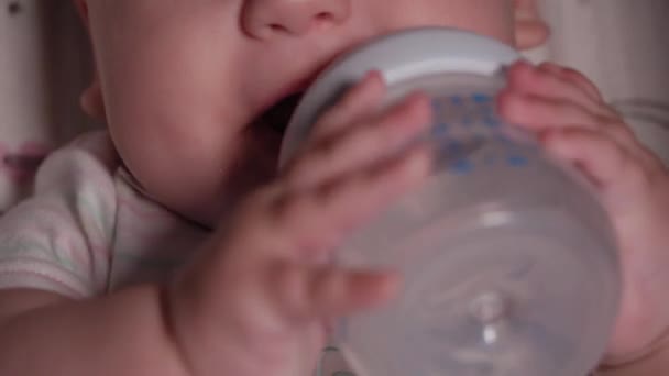 Kojenec, dětství, emoční koncept - Extrémní detailní záběr usmívající se tváře hnědookého novorozence bdělého bezzubé dítě 7 měsíců staré pít vodu z láhve s bradavkou ležící v bílém obleku v kočárku — Stock video