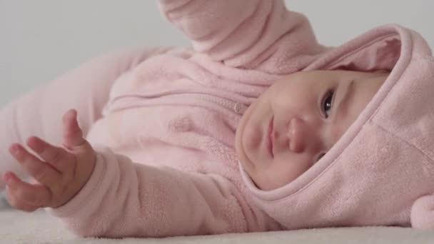 Criança, conceito de infância - close-up de sorrir feliz gordo rosto gordinho de olhos castanhos engraçado de criança recém-nascida acordada. toothless 7 meses bebê grimaces, fecha os olhos mentira em cama macia em rosa vira sobre na barriga. — Vídeo de Stock