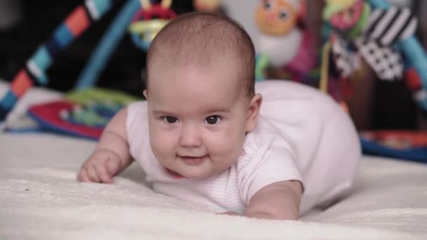 Spädbarn, barndom, föräldraskap, utveckling, medicin och hälsa koncept - front view närbild ansikte knubbig nyfödd baby glad vakenhet i rosa body suit leende och göra grimaser ligger på magen. — Stockvideo