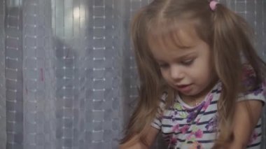 Çocukluk, yaratıcılık, doğa, ilkbahar, yaz konsepti - 3-4 yaşındaki sevimli küçük kızın yakın çekimi pencere camında akrilik renkler çiziyor. Anaokulu resim manzarası: güneş, ağaç, bulut, yağmur, çiçek