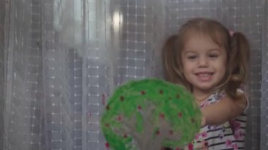 Çocukluk, yaratıcılık, doğa, ilkbahar, yaz konsepti - 3-4 yaşındaki sevimli küçük kızın yakın çekimi pencere camında akrilik renkler çiziyor. Anaokulu resim manzarası: güneş, ağaç, bulut, yağmur, çiçek