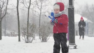 Kış, tatil, oyunlar, aile kavramları - iki mutlu anaokulu çocuğu, anneleriyle birlikte şapka ve eldiven takmış çocuklar, soğuk mevsimde kartopu oynuyorlar.