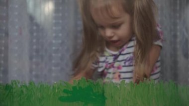 Çocukluk, yaratıcılık, doğa, ilkbahar, yaz konsepti - 3-4 yaşındaki sevimli küçük kızın yakın çekimi pencere camında akrilik renkler çiziyor. Anaokulu resim manzarası: güneş, ağaç, bulut, yağmur, çiçek