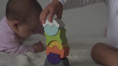 Çocukluk, aile, izolasyon, inşaat konsepti - 2 küçük mutlu çocuk yatağa oturmuş ahşap piramit inşa ediyor. 6-9 aylık yeni doğmuş kız çocuğu ve 2-3 yaşındaki oğlan evde motor becerileri için oyun oynuyorlar..