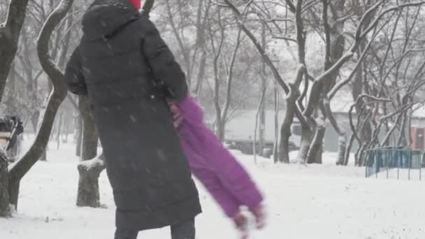 Зима, каникулы, игры, семейные концепции - счастливый дошкольный ребенок дочка девочка убежать играть сделать снежок с мамой, весело вращаться в снегопад холодный сезон погода в парке на открытом воздухе — стоковое видео