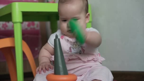 Bébé, concept d'enfance - gros plan de souriant heureux dodu drôle tout-petit enfant potelé nouveau-né réveillé 8 mois bébé fille assis ramper sur le tapis jeu de sol avec pyramide multicolore dans la salle de jeux à l'intérieur à la maison — Video