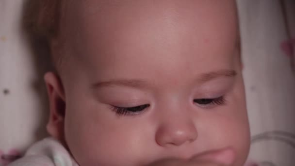 Bebé, infancia, concepto de emoción - Primer plano extremo de la cara sonriente del recién nacido de ojos marrones despierto bebé sin dientes 7 meses de edad beber agua del biberón con pezón acostado en traje de cuerpo blanco en el cochecito — Vídeo de stock